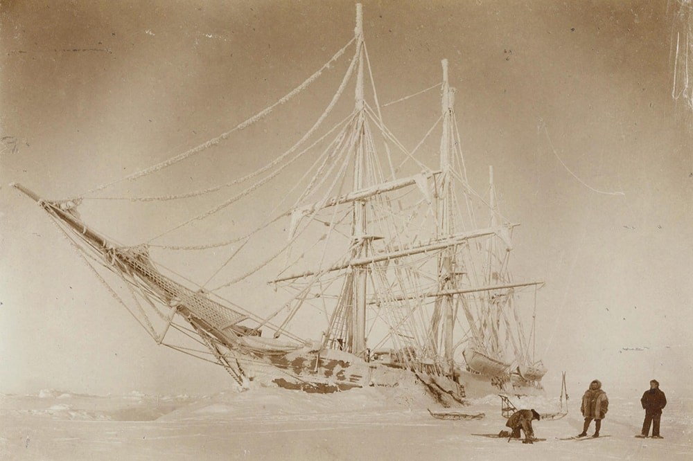 Speia tone photo of the Belgica stuck in ice with three crew members in the foreground