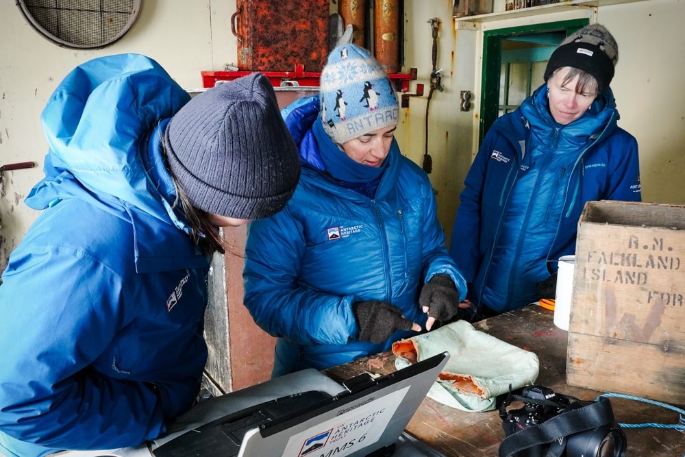 Ruth and two conservators inside Detaille hut with a laptop