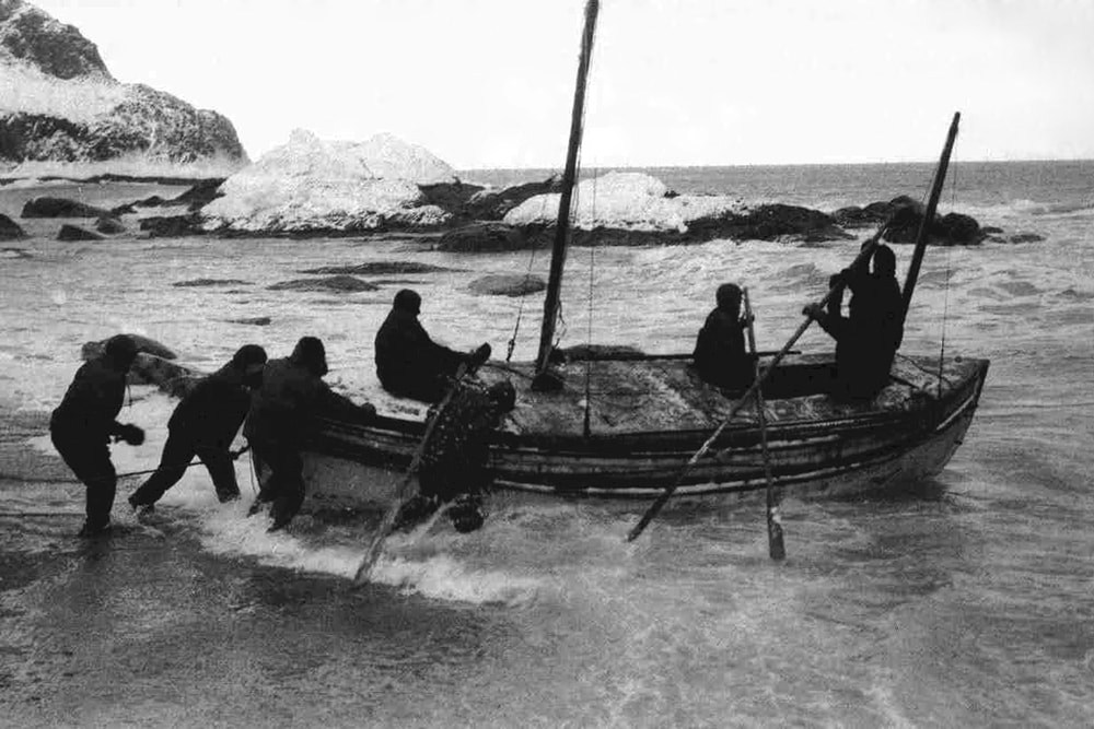 A B&W photo of sailors launching the James Caird lifeboat in waves
